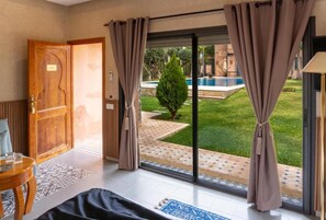 Una habitación con una cama, una puerta de madera, vista a una piscina y una puerta de cristal que da al exterior.