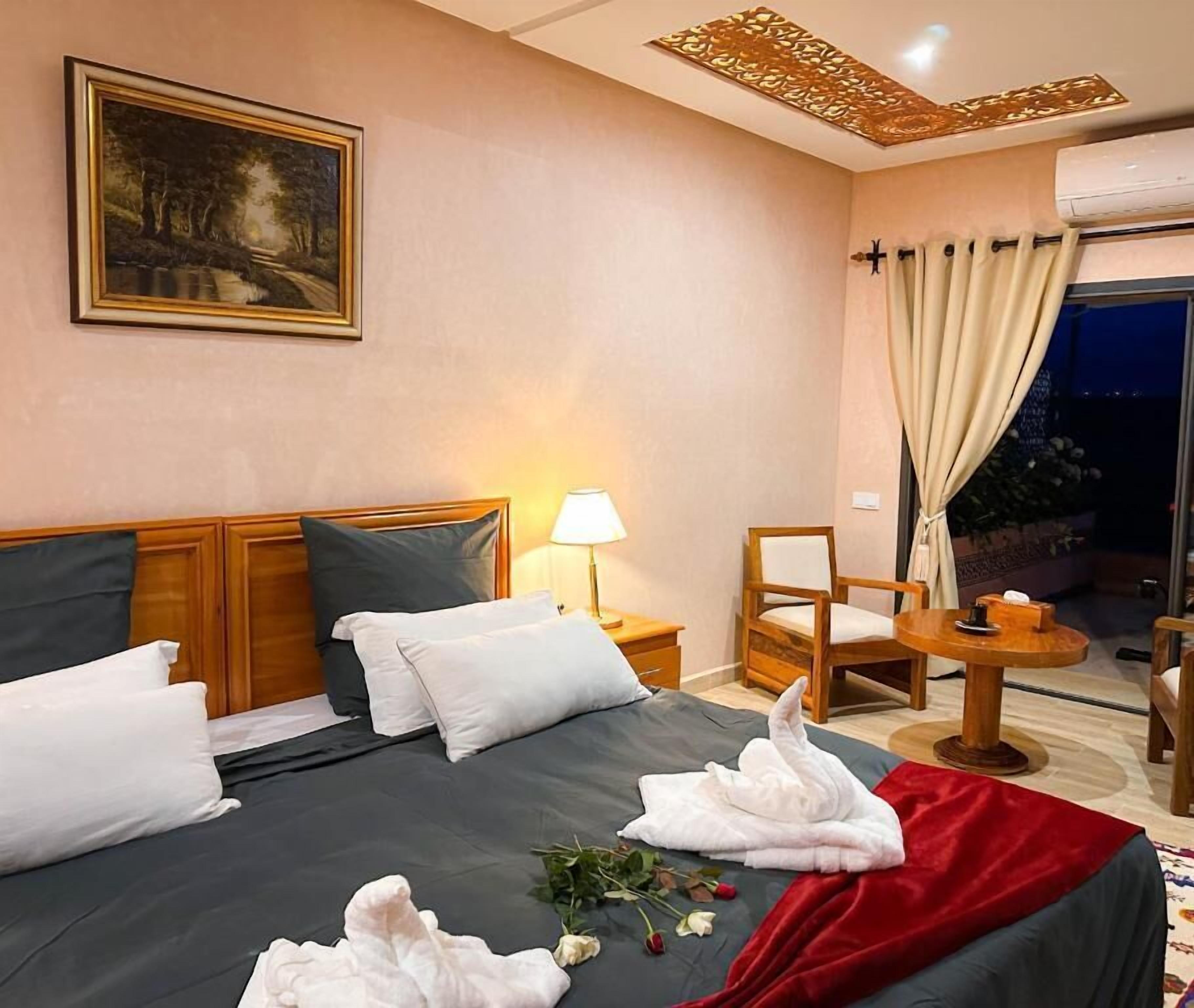 A hotel room with a bed, a chair, a small table, a lamp, and a painting on the wall.