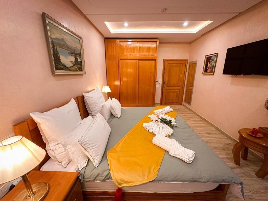 A hotel room with a bed, a bedside table with a lamp, a TV, and a wooden wardrobe.