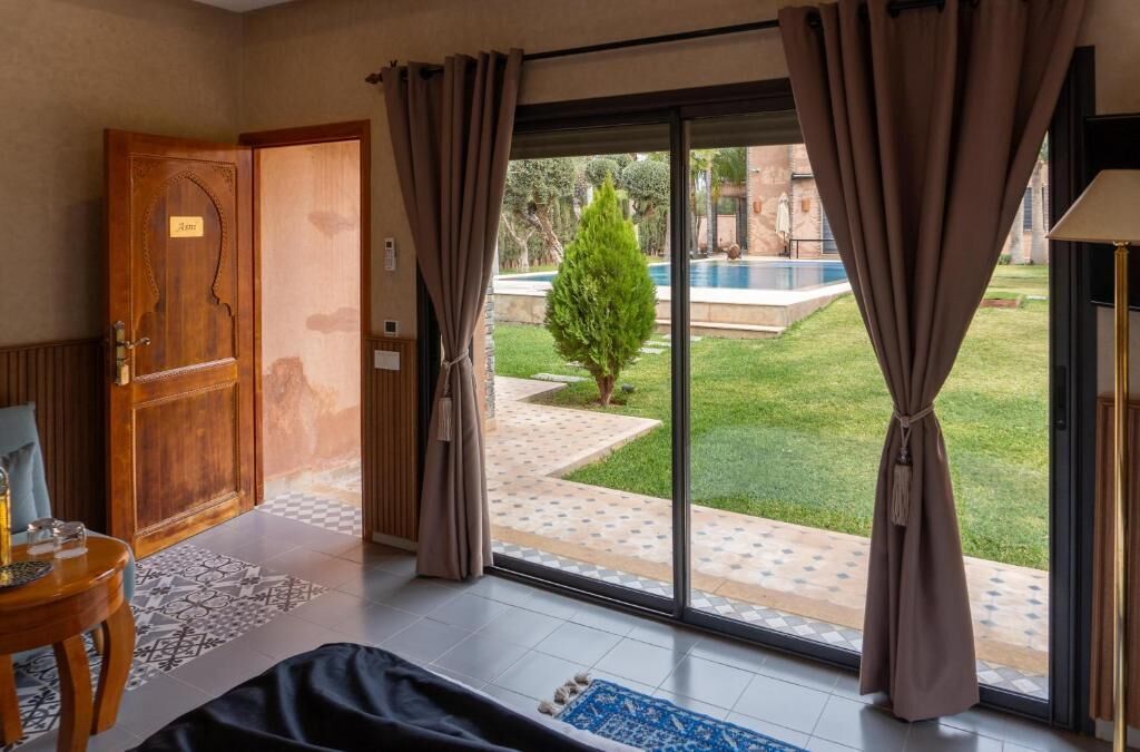 A room with a large sliding glass door leading to a pool area, a wooden door with a nameplate, and a small table with a lamp.