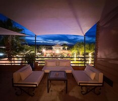 Un área de estar al aire libre con un sofá y una mesa, bajo un toldo, con vistas a un edificio de techo abovedado.