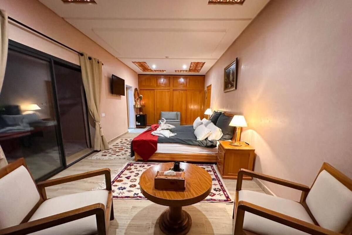 Ett hotellrum med en säng, ett skrivbord, två stolar, en tv och ett fönster med gardiner.