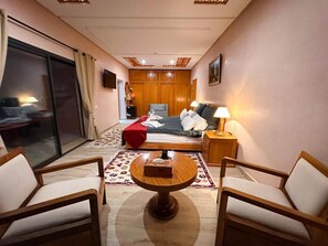 A hotel room with a bed, a desk, two chairs, a TV, and a window with curtains. - Atlas Front (Sidi Abdallah Ghiat)