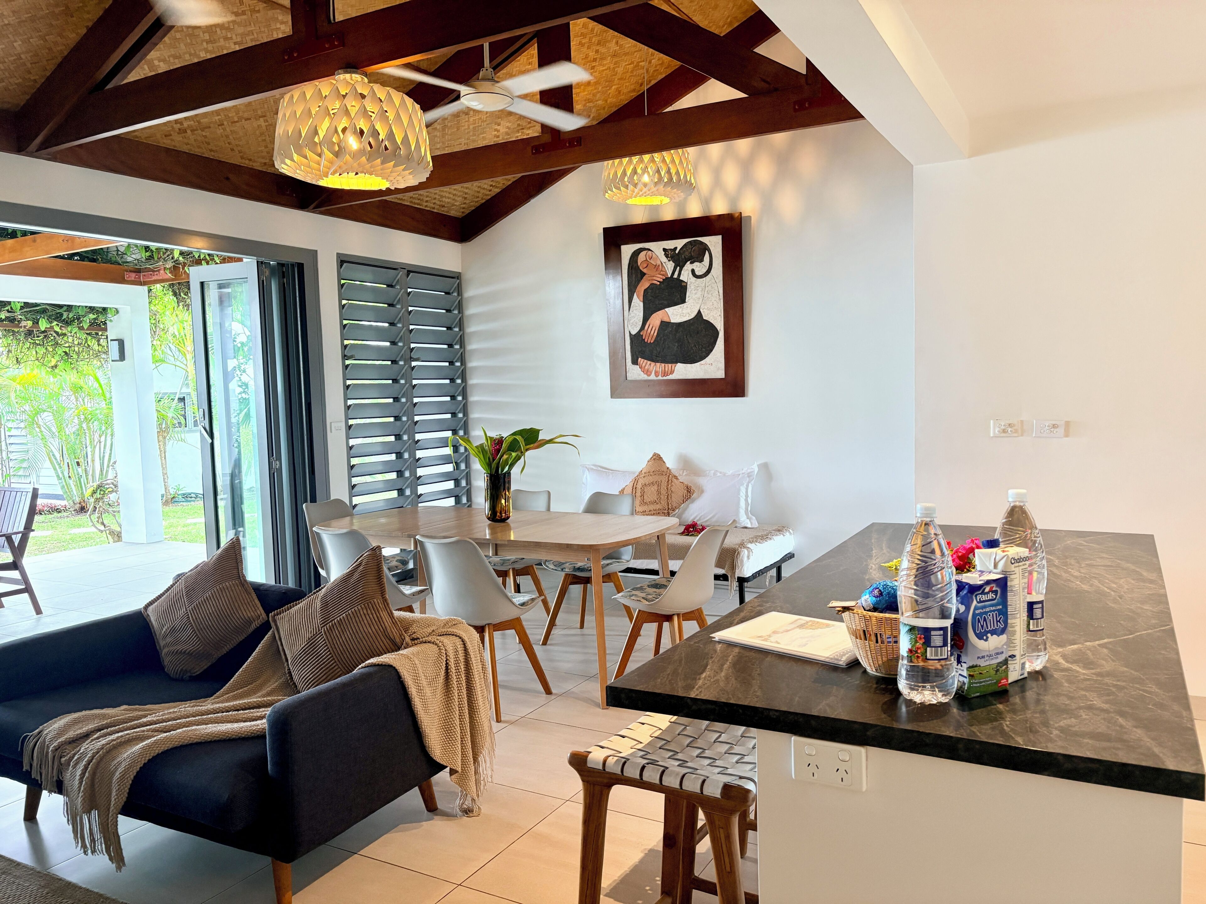 A modern kitchen with a dining area, a sofa, and a coffee table with milk and water bottles.