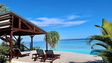 A wooden gazebo with lounge chairs overlooking a clear blue ocean.