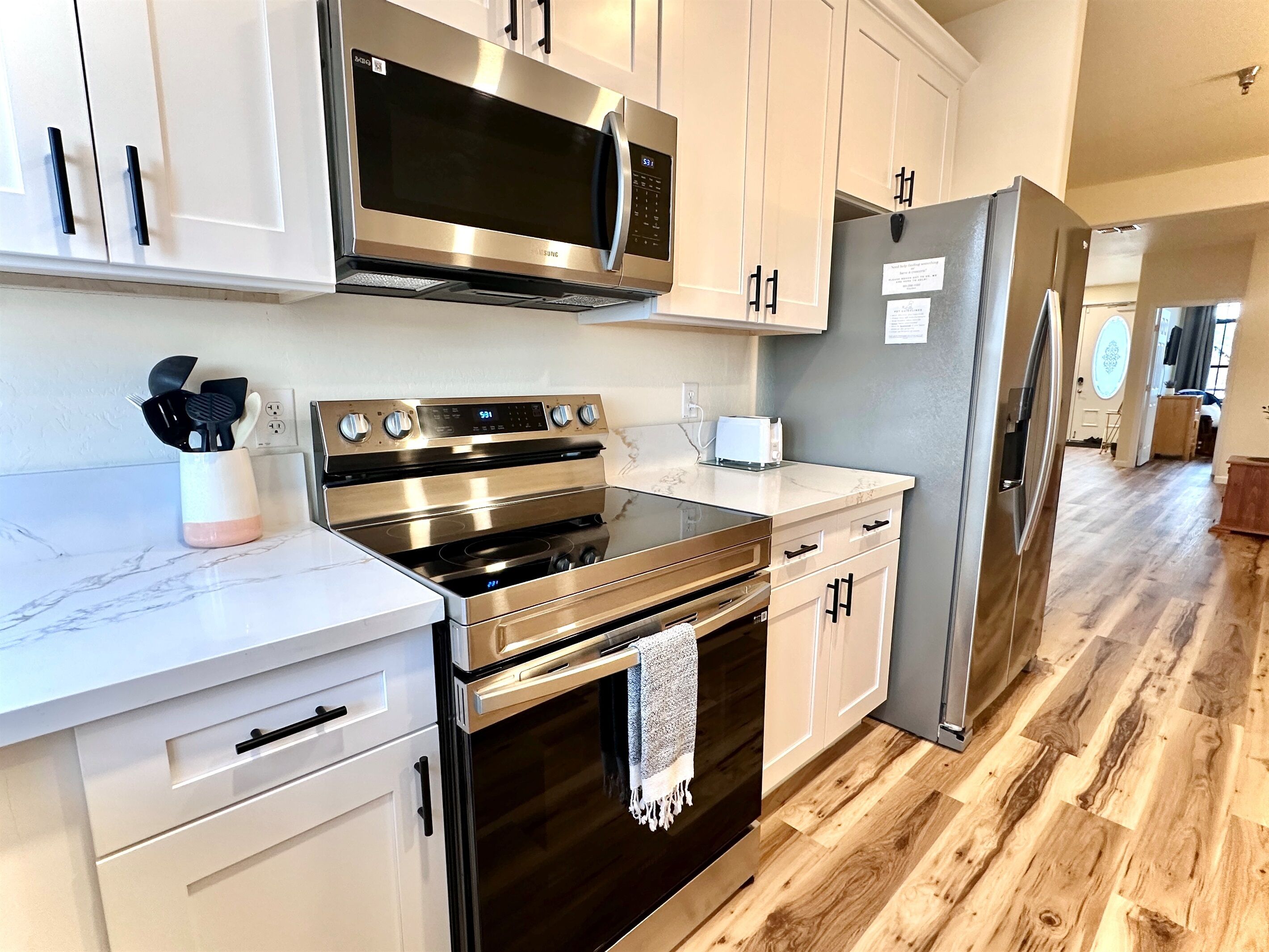 A modern kitchen with stainless steel appliances, white cabinetry, and a wooden floor.