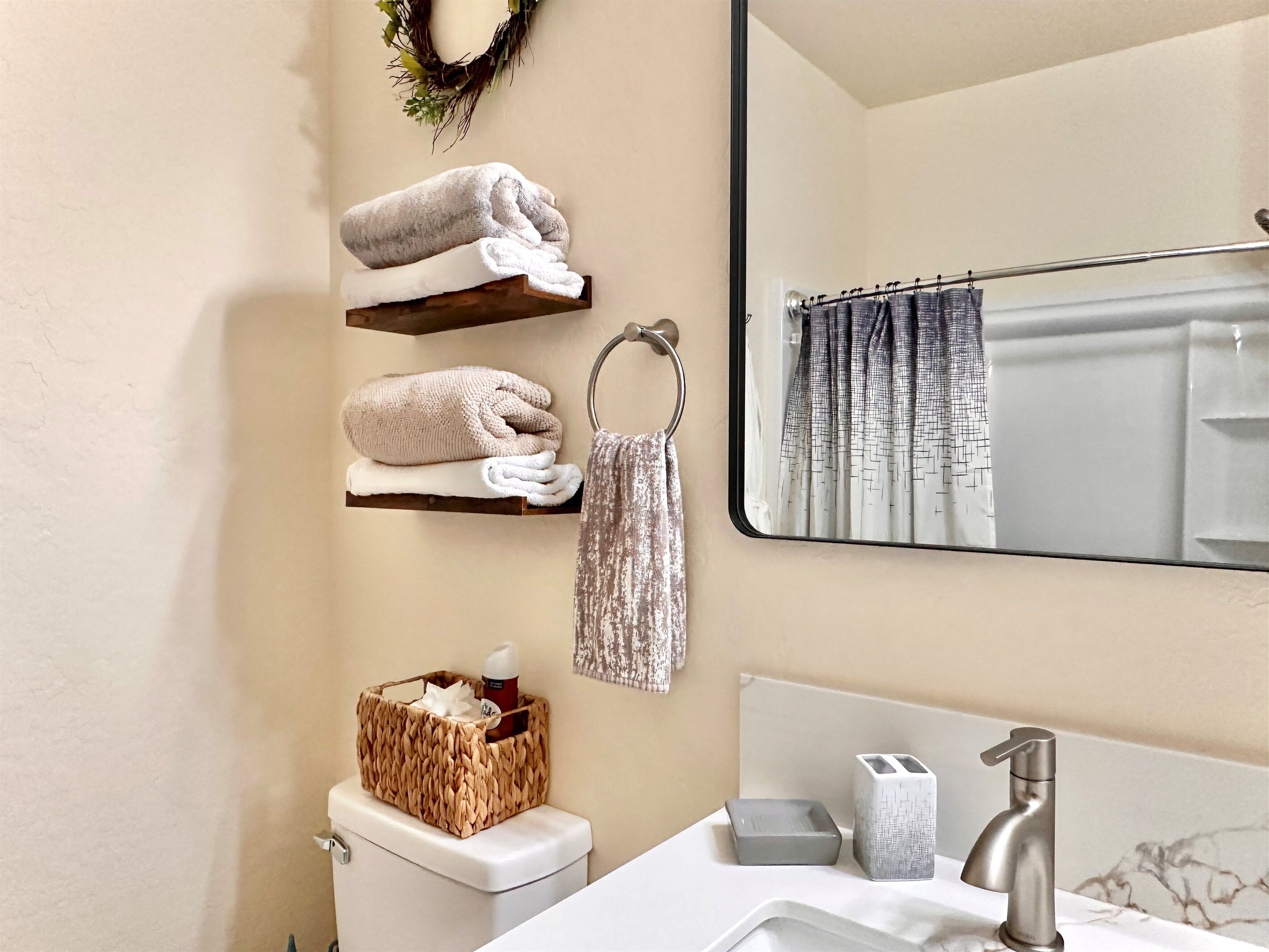 A bathroom with a toilet, a sink with a mirror, a towel rack with towels, a basket with toiletries, and a shower curtain.
