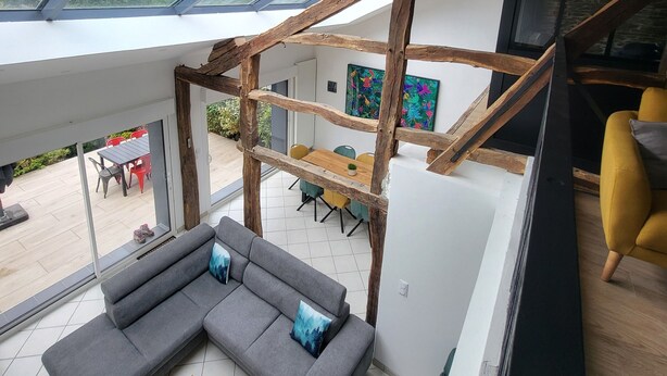 Um interior moderno com área de estar estilo loft, espaço para refeições e escadaria com vigas de madeira aparentes.