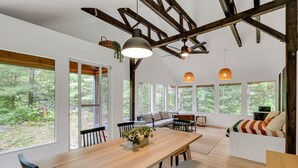 A spacious room with a large wooden dining table, multiple seating options, and large windows offering a view of the forest.