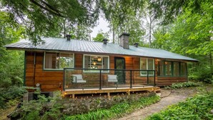 A cabin with a wooden exterior, large windows, and a deck with outdoor lighting.