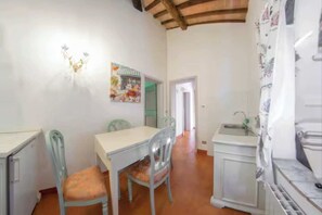 A room with a dining table, two chairs, a small kitchen area, and a door leading to another room. - Geraneo 1 - comfortable apartment on the second floor (Poggio delle Corti)