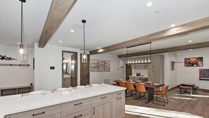 Una cucina moderna con una grande isola, travi in legno, luci a sospensione e un'area pranzo con sedie arancioni.