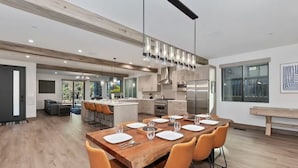 Une cuisine moderne dotée d’un îlot central, d’appareils électroménagers en acier inoxydable et d’un coin repas avec des chaises orange et une table en bois.
