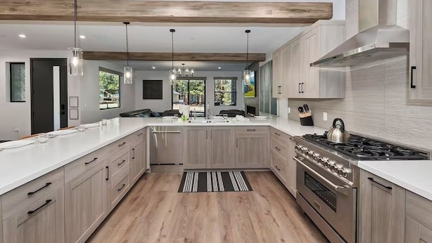 Une cuisine moderne avec des meubles en bois clair, une cuisinière en acier inoxydable et des luminaires suspendus.
