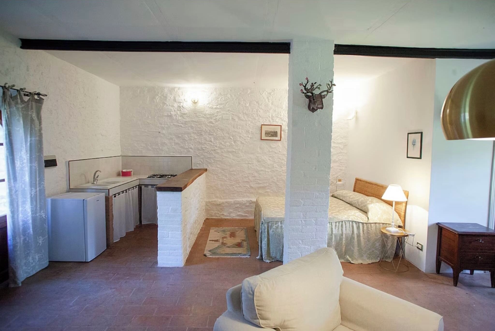 Un espacio habitable compacto con kitchenette, cama, sofá y una mesita con lámpara.