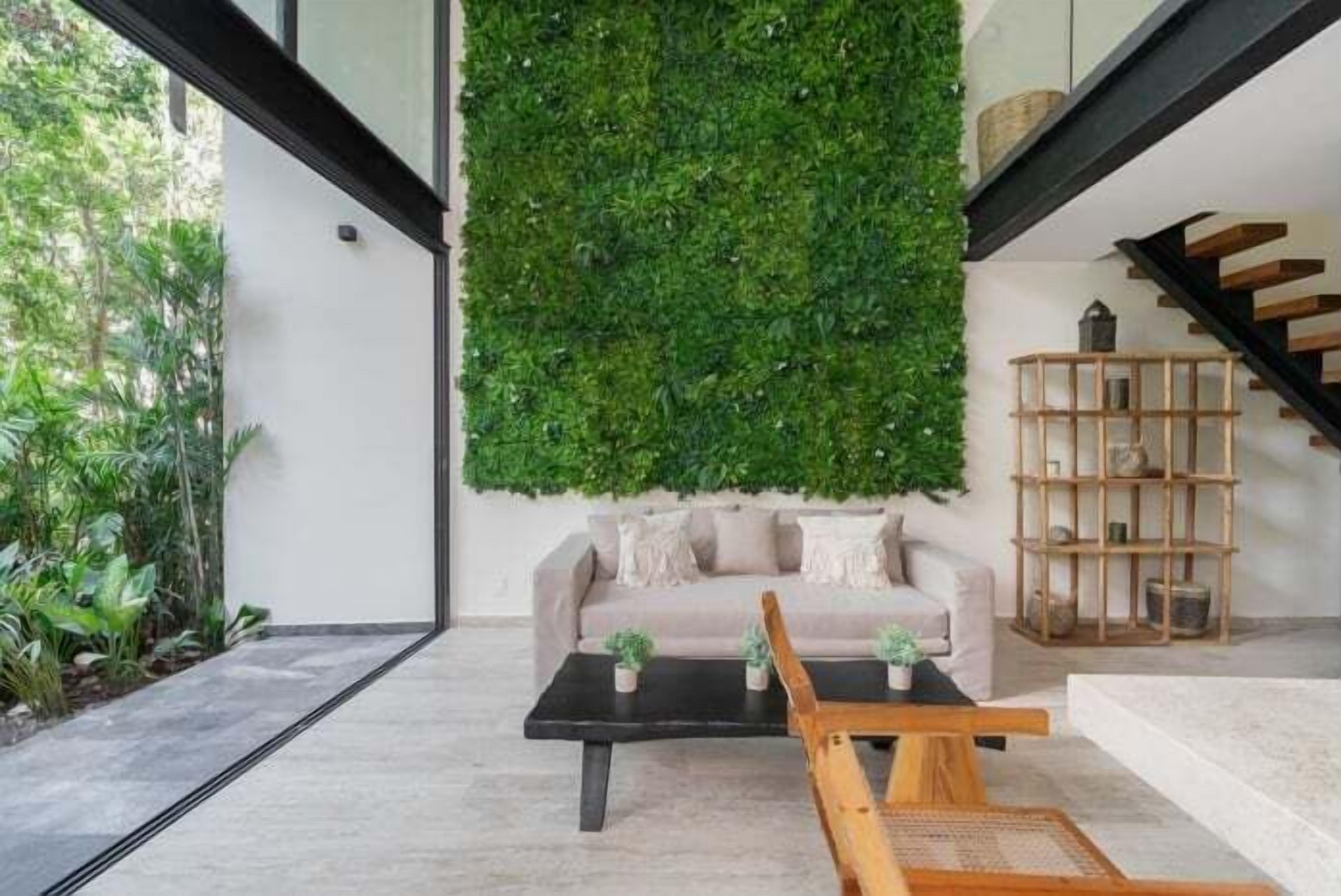 Una sala de estar moderna con un jardín vertical verde, un sofá color beige, una mesa de centro de madera y una estantería de madera.