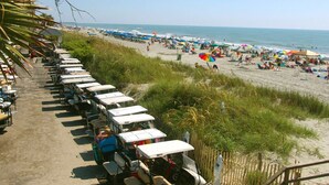 A beach with rows of parked vehicles and beachgoers under umbrellas. - Delightful 5-bedroom house within Oceanside Village in Surfside Beach (Surfside Beach)
