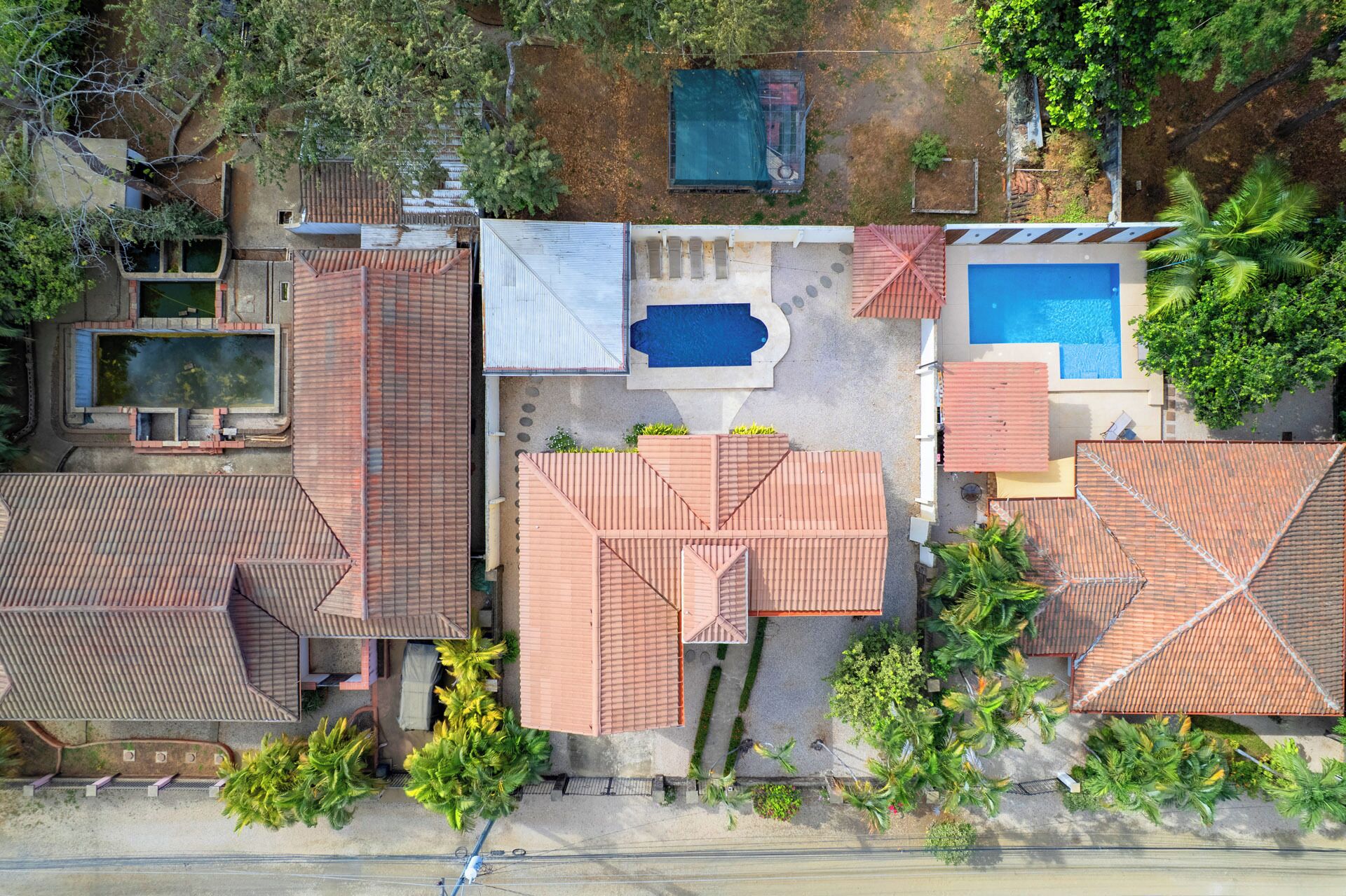 An aerial view of a residential area with multiple houses, each featuring a swimming pool, tiled roofs, and surrounding greenery.