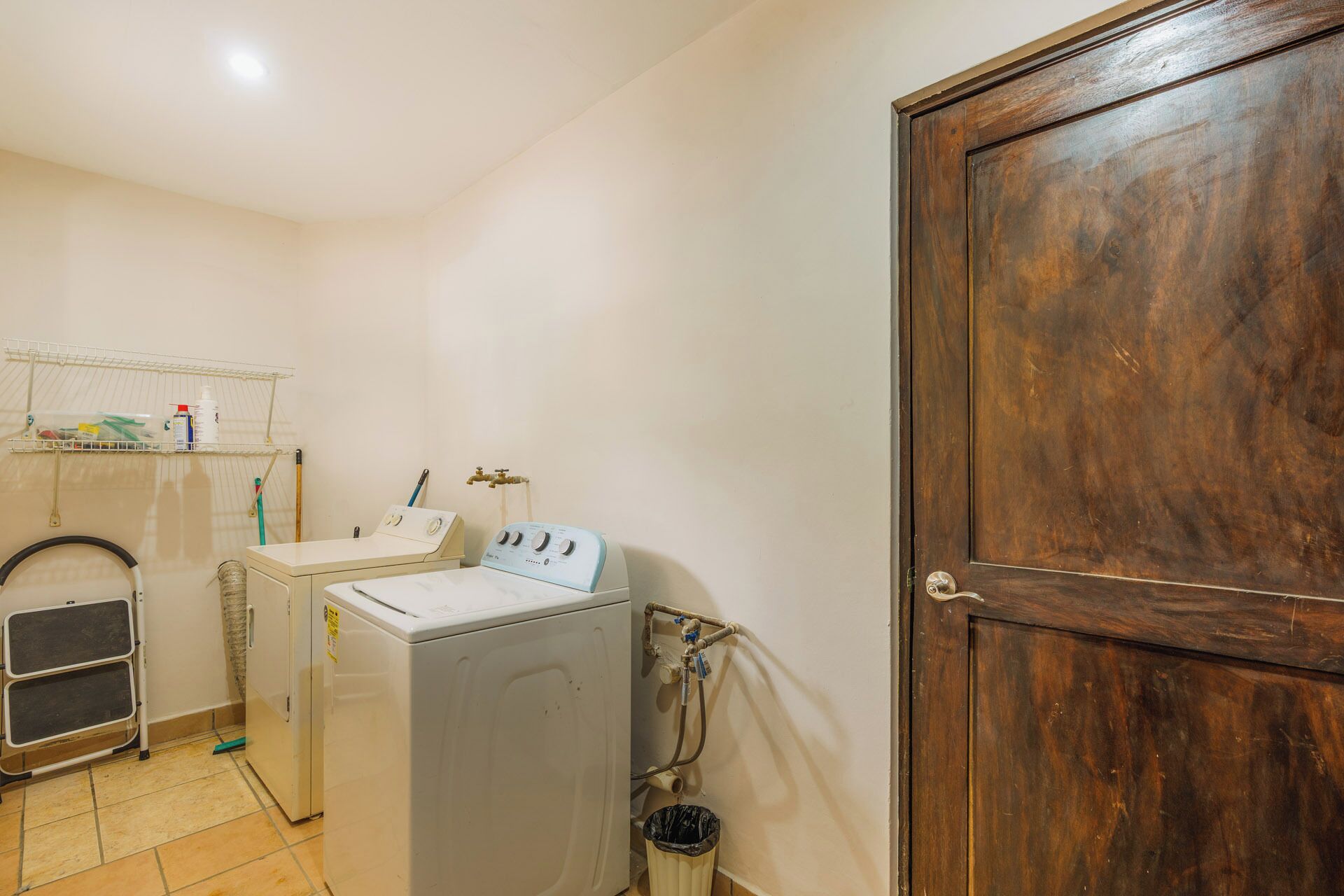 A laundry room with a washing machine, dryer, and a wooden door.