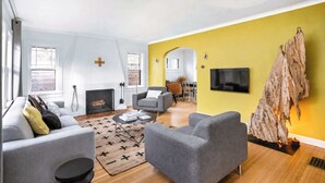 Una sala de estar con chimenea, sofás grises, una pared de acento amarilla y un televisor montado.