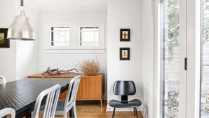 Un comedor moderno con una mesa de madera, sillas blancas y una silla negra. Hay dos ventanas con marcos blancos y una puerta que da al exterior.