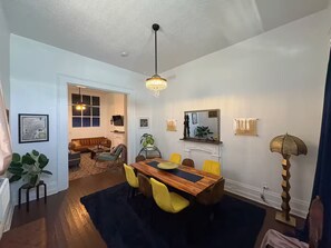 A dining area with a wooden table, yellow chairs, and a chandelier. There is a sofa and a coffee table in the background. - Truly New Orleans Enjoyable 3-bedroom house with AC in welcoming New Orleans (New Orleans)