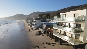 Hotel a primera línia de platja, amb diversos balcons que donen a l'oceà, una platja de sorra i un paisatge amb hills al fons.