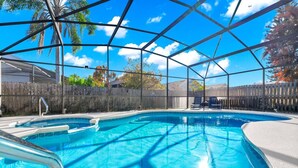 A clear blue pool with a wooden deck and chairs, surrounded by a wooden fence and trees. - Waterfront Oasis – 4BR Pool & Spa (Kissimmee)