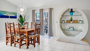 A dining area with a wooden table and chairs, a hanging light fixture, and a unique circular shelving unit with decorative items. - Waterfront Oasis – 4BR Pool & Spa (Kissimmee)