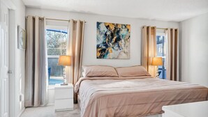 A bedroom with a bed, two bedside tables, a window with curtains, and a painting on the wall. - Waterfront Oasis – 4BR Pool & Spa (Kissimmee)