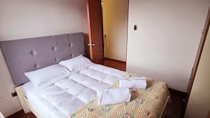 A neatly made bed with a grey headboard, a white duvet, and a crocheted throw blanket. - Bright and comfortable apartment close to Real Plaza - Pet friendly (Cusco)