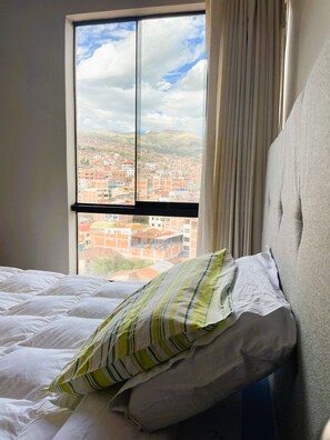 A hotel room with a bed, a window with a cityscape view, and a curtain. - Bright and Cozy Apartment Near Real Plaza – Pet-Friendly   (Cusco)