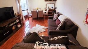 A living room with a sofa, a TV, a dining table with chairs, a rug, and a bookshelf. - Bright and comfortable apartment close to Real Plaza - Pet friendly (Cusco)