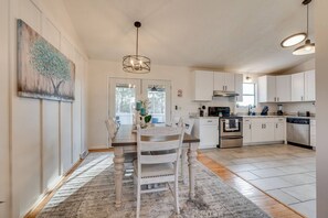 A modern kitchen with white cabinets, stainless steel appliances, and a dining area with a wooden table and chairs. - Peaceful Valley Hideaway—a roomy & fun, family-friendly home in Jonesborough, TN (Jonesborough)