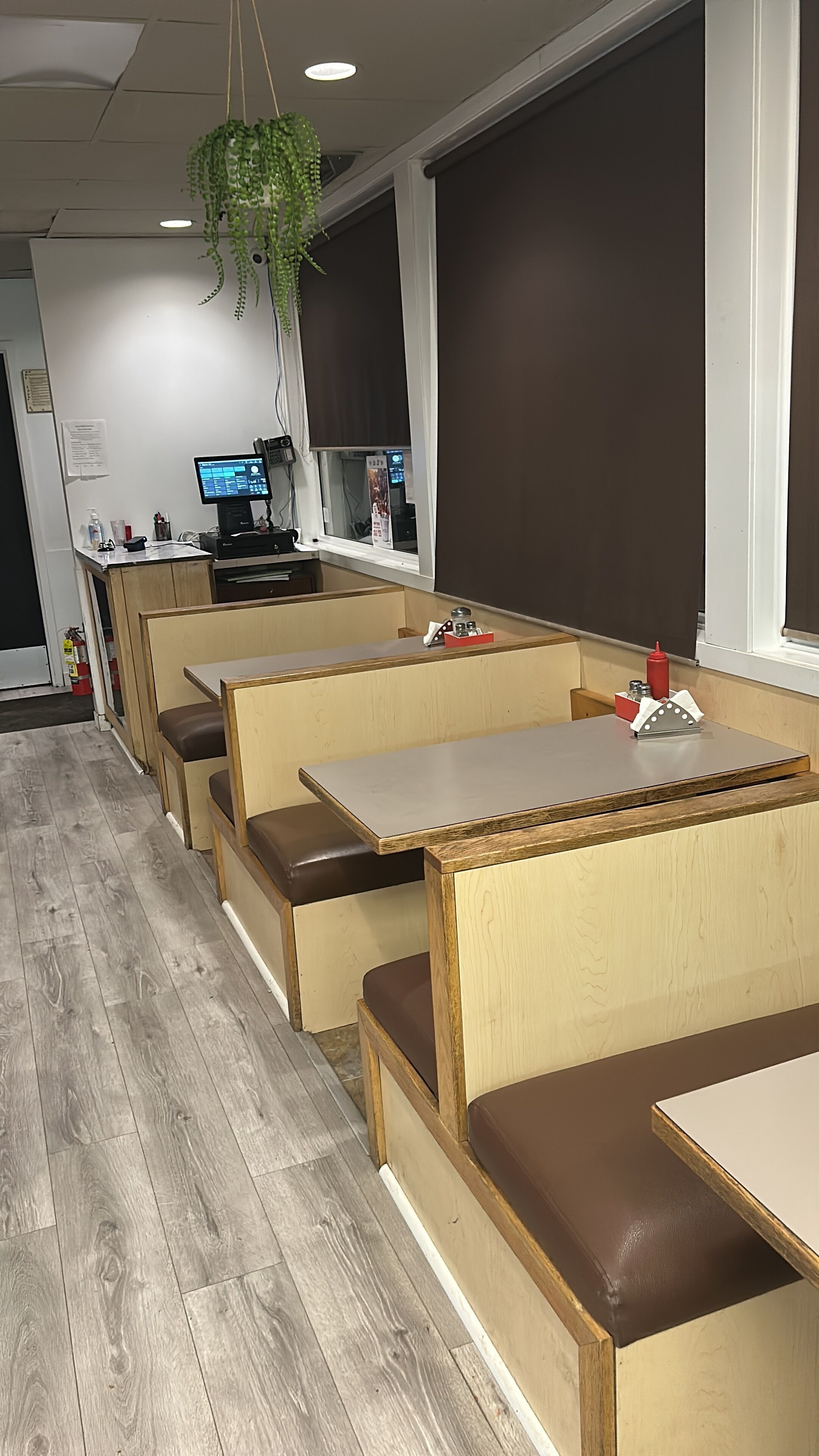 L'intérieur d'un restaurant avec des banquettes en bois, un écran d'ordinateur et une plante suspendue.
