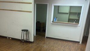 A room with wooden flooring, a stool, a window with a shelf, and a door leading to another room. - Barnays Motel (Letellier)