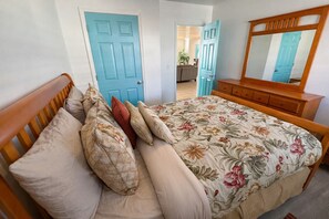 A bedroom with a bed, wooden headboard, floral bedspread, and a wooden dresser with a mirror. - Bid-A-Wee Palms - Sleeps 12 - Close to the Beach (Panama City Beach)