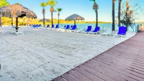 Ein Strand mit Holzsteg, Liegestühlen und Palmen.
