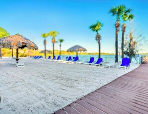 Ein Strand mit Holzsteg, Liegestühlen und Palmen.