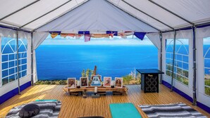 A tent with a wooden floor, a table with framed pictures, and a view of the ocean. - Kona Ocean Paradise with Pool and Hot Tub (Captain Cook)