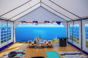 A tent with a wooden floor, a table with framed pictures, and a view of the ocean. - Kona Ocean Paradise with Pool and Hot Tub (Captain Cook)