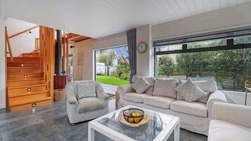 Una sala de estar moderna con una escalera, un juego de sofá, una mesa de centro con fruta y un ventanal que ofrece vistas de follaje.
