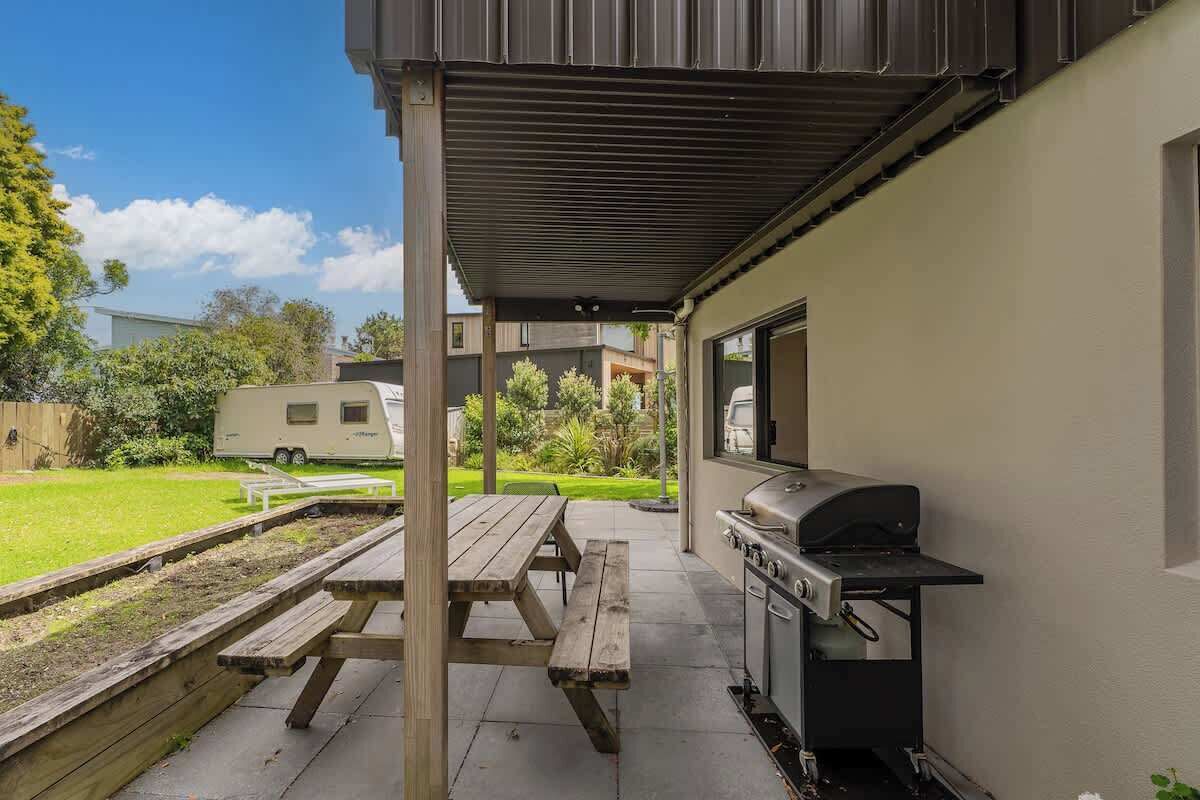 Une terrasse couverte équipée d’un barbecue, d’une table de pique-nique et offrant une vue sur un quartier résidentiel.