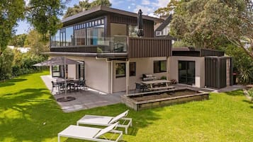 Una casa moderna de dos pisos con un patio, mobiliario exterior y un césped bien cuidado.