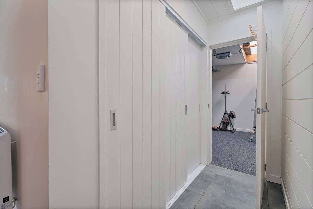 A hallway with white paneling, a ceiling light fixture, and a door leading to another room.