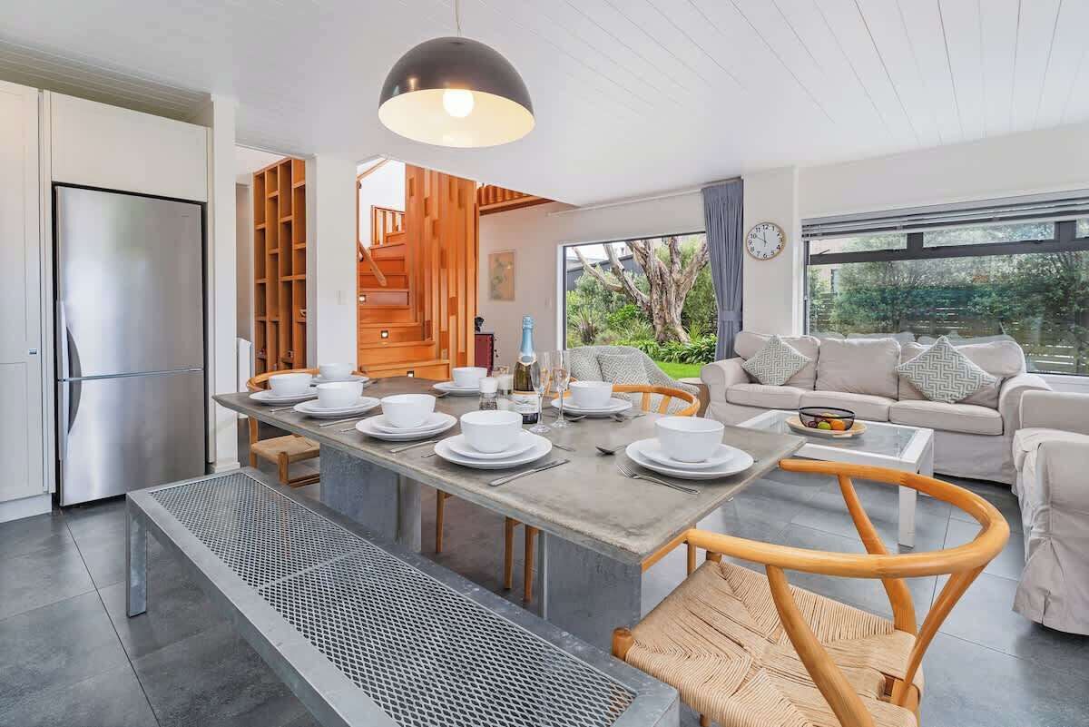 Una cocina moderna con refrigerador empotrado, un área de comedor con una mesa grande dispuesta para cuatro personas, y una sala de estar con sofá y mesa de centro.