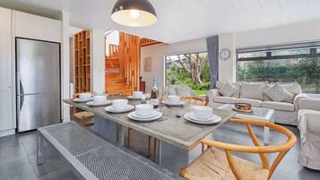 Una cocina moderna con refrigerador empotrado, un área de comedor con una mesa grande dispuesta para cuatro personas, y una sala de estar con sofá y mesa de centro.