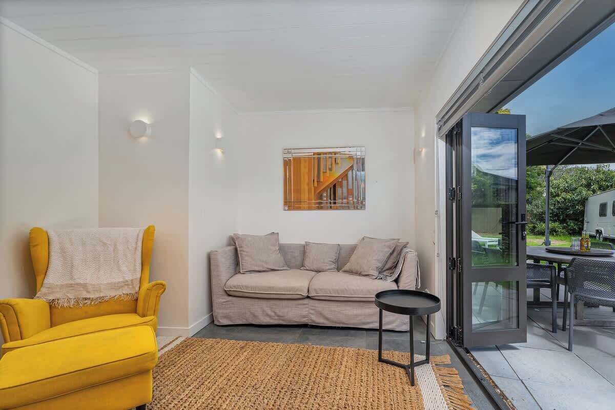 Un salon moderne avec un fauteuil jaune, un canapé gris et une porte en verre donnant sur un espace extérieur.