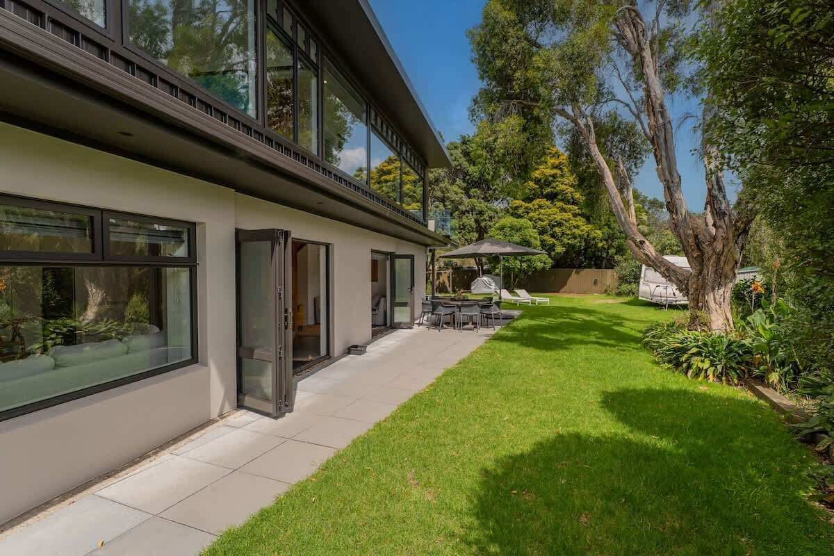A modern house with large windows, a patio with a table and chairs, and a well-maintained lawn.