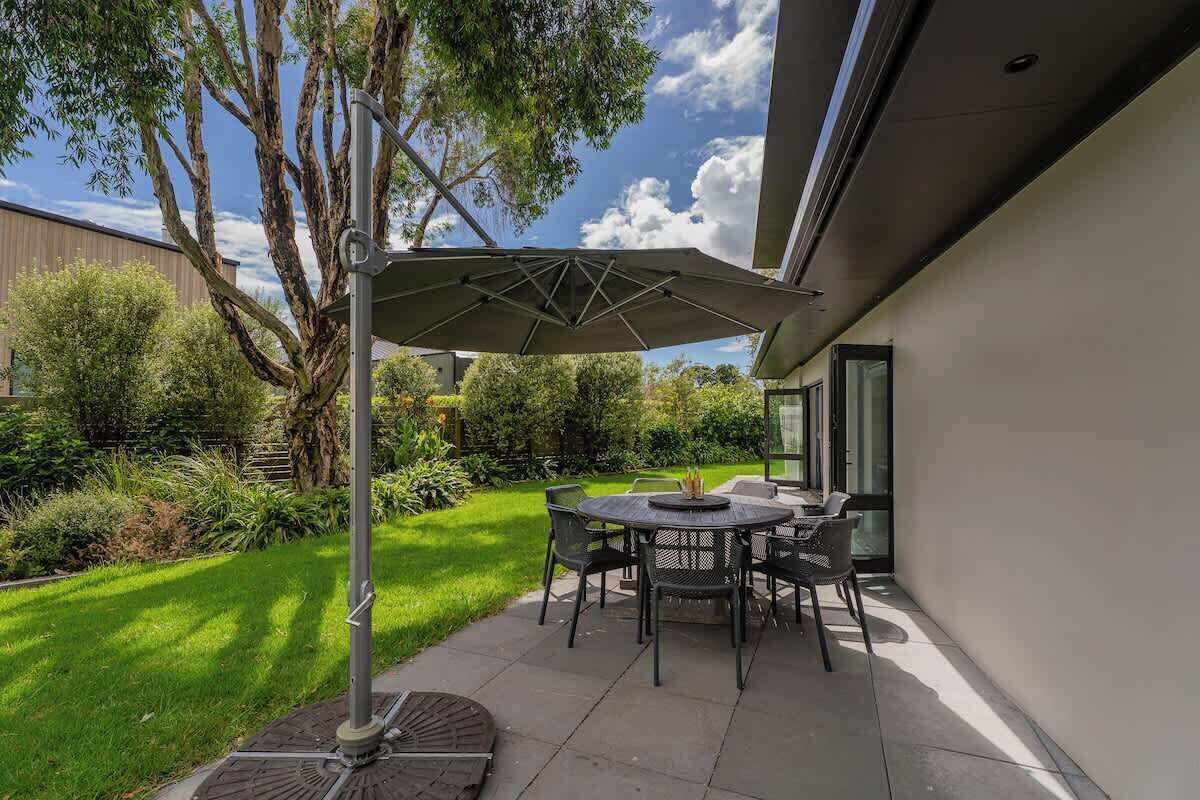 An outdoor patio with a table and chairs, a large umbrella, and a tree.